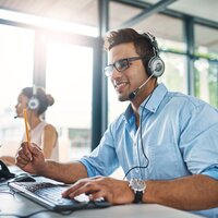 © iStock-1132874986_PeopleImages (Cropped shot of a handsome young man working in a call center with a female colleague in the background)