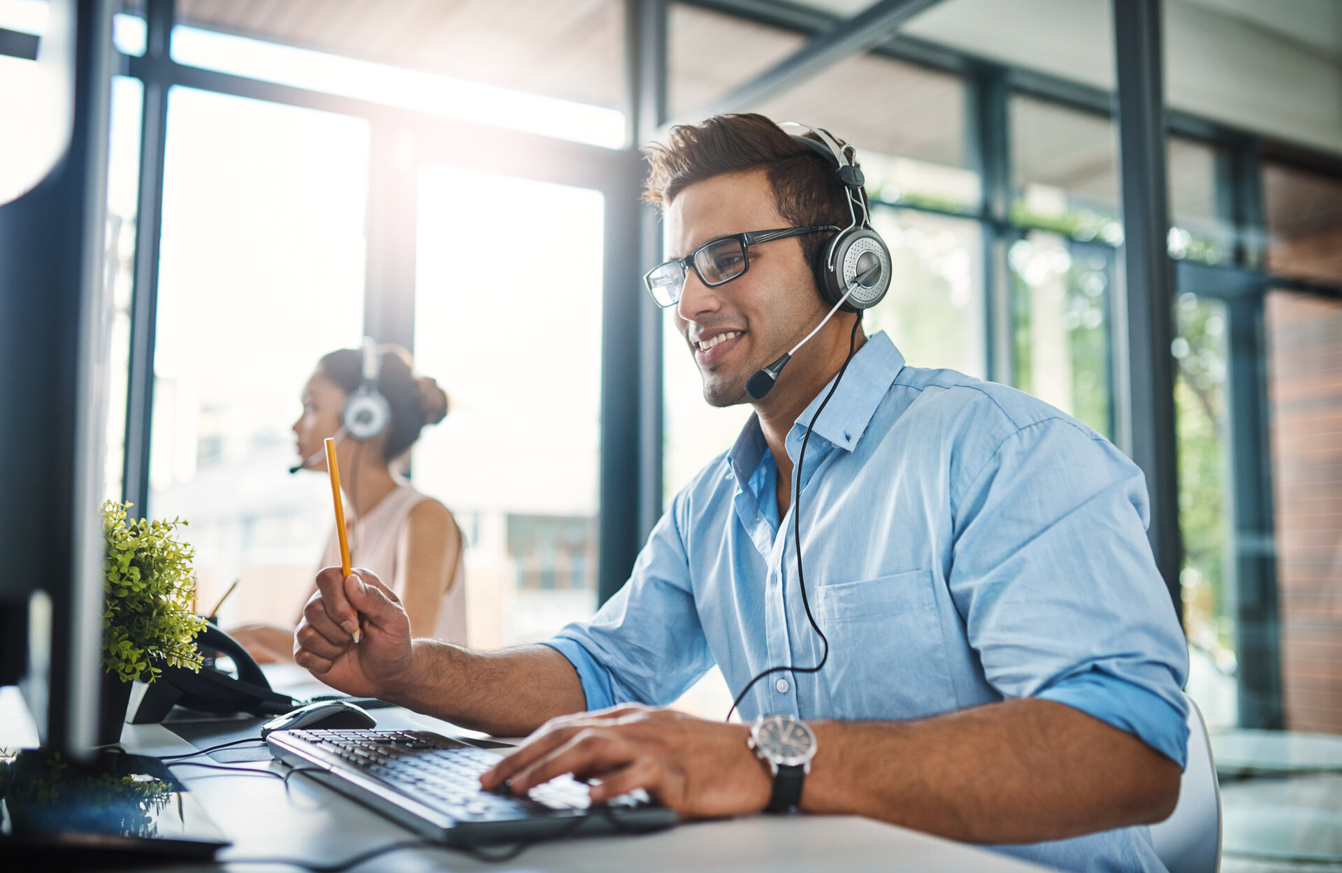 © iStock-1132874986_PeopleImages (Cropped shot of a handsome young man working in a call center with a female colleague in the background)